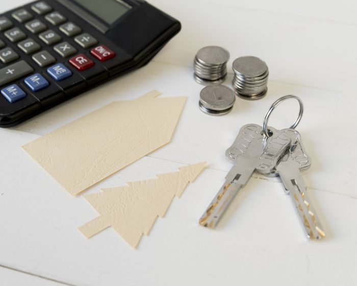 calculator-coins-stack-keys-with-house-tree-paper-cutout-white-wooden-table