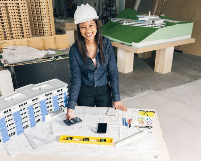 happy-african-american-lady-safety-helmet-standing-near-model-building (Demo) (Demo)