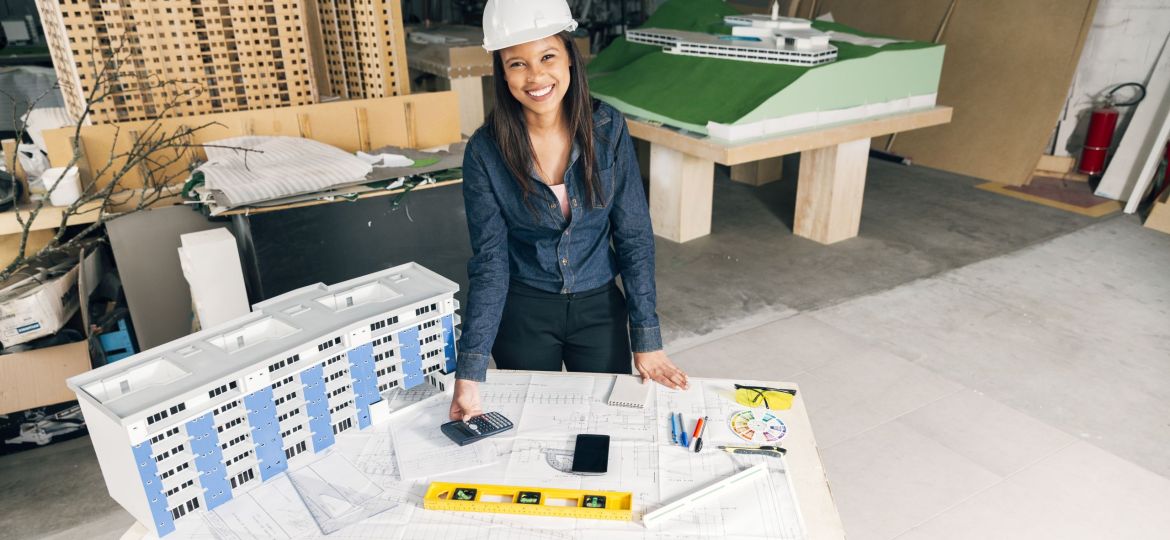 happy-african-american-lady-safety-helmet-standing-near-model-building (Demo) (Demo)